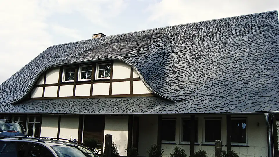 Wood-framed window set in dark slate-tiled roof with copper edging on a building under scaffolding.
