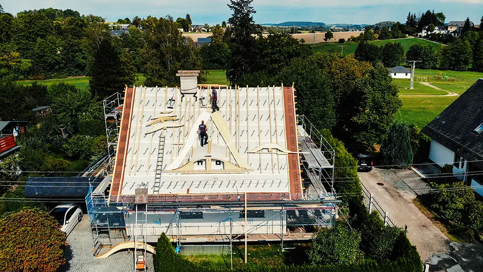 Copper roof structure with vertical supports viewed from above with scaffolding and trees in background.