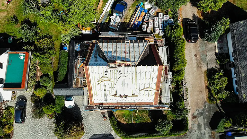 Copper roof structure with vertical supports viewed from above with scaffolding and trees in background.
