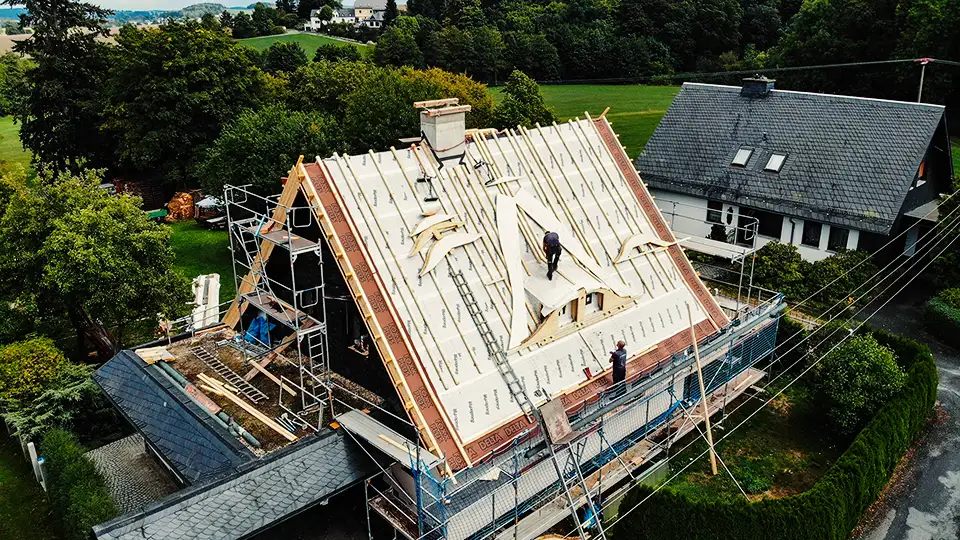 Copper roof structure with vertical supports viewed from above with scaffolding and trees in background.