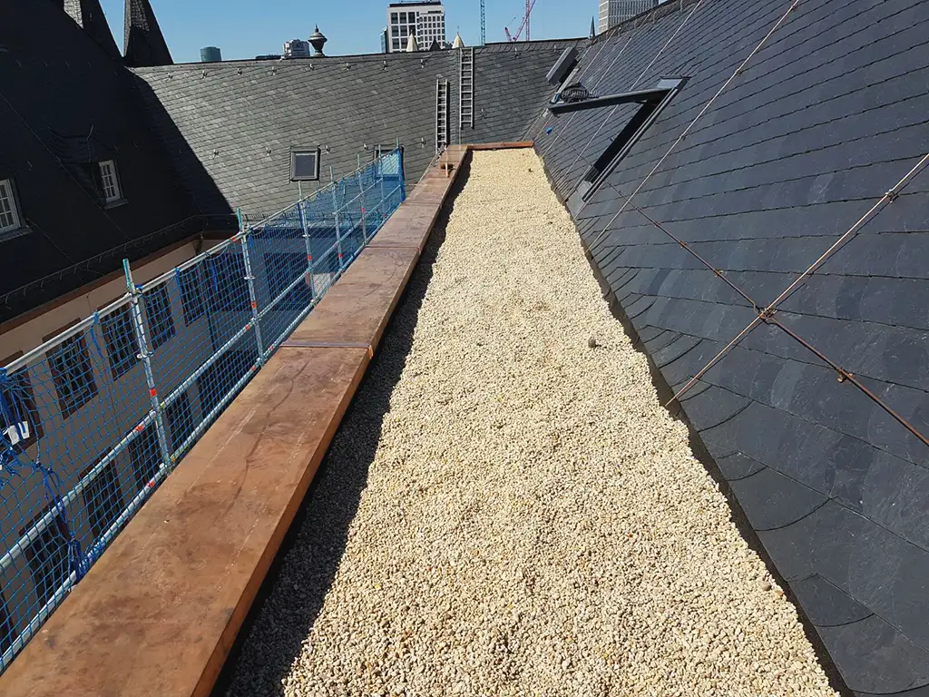Curved dark slate roof with an attached rusty vertical pipe or antenna against a partly cloudy sky.