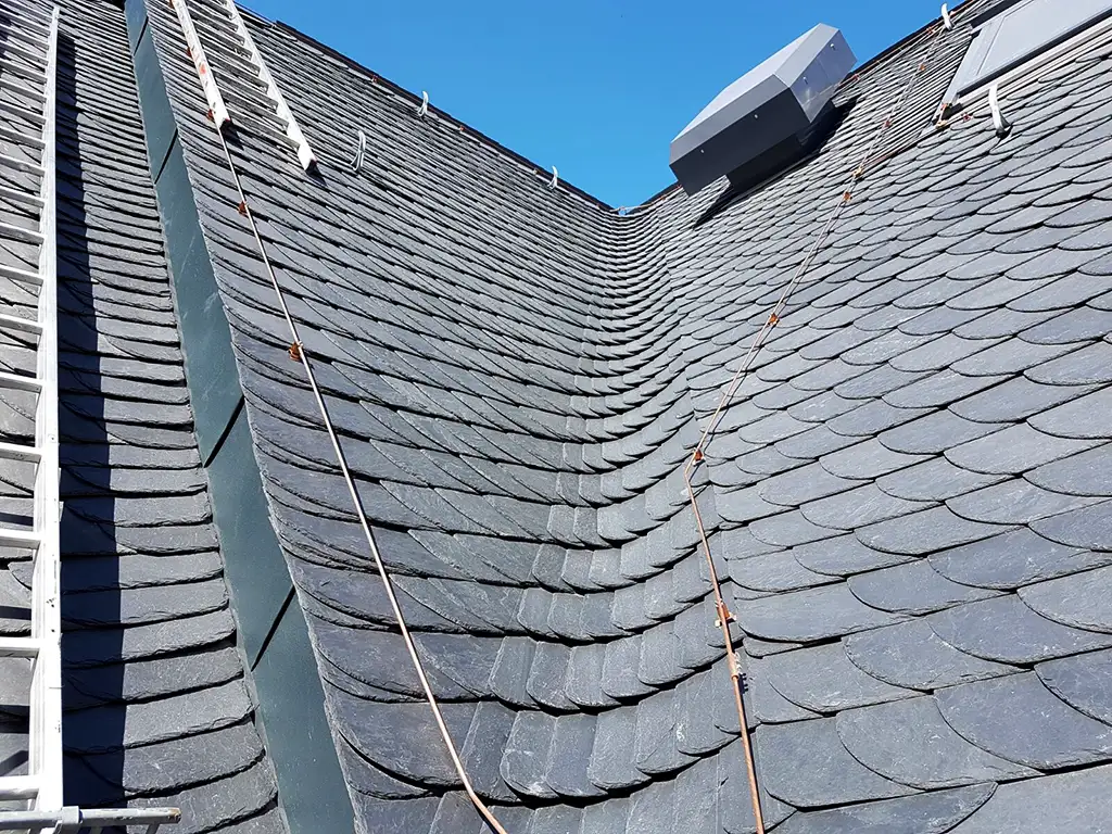 Copper roof structure with vertical supports viewed from above with scaffolding and trees in background.