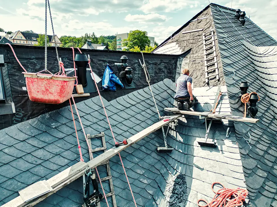 Curved dark slate roof with an attached rusty vertical pipe or antenna against a partly cloudy sky.