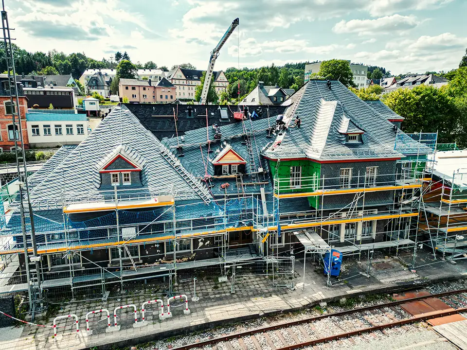 Curved dark slate roof with an attached rusty vertical pipe or antenna against a partly cloudy sky.