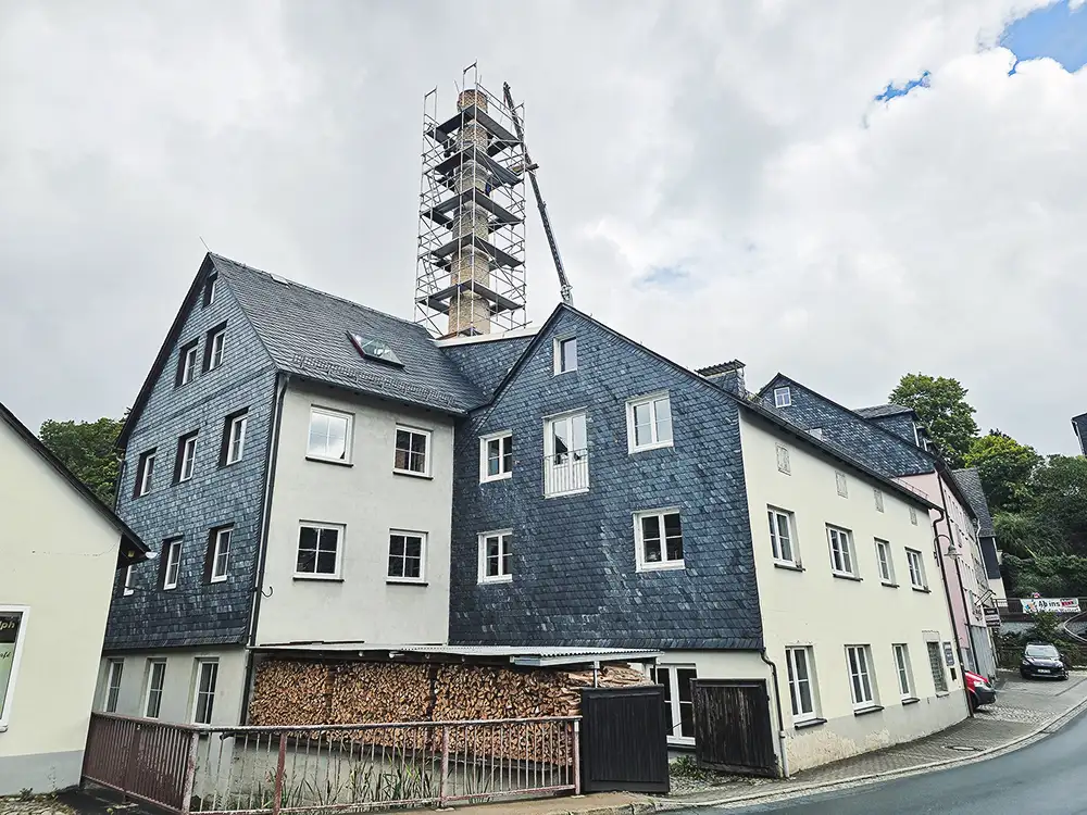 Curved dark slate roof with an attached rusty vertical pipe or antenna against a partly cloudy sky.