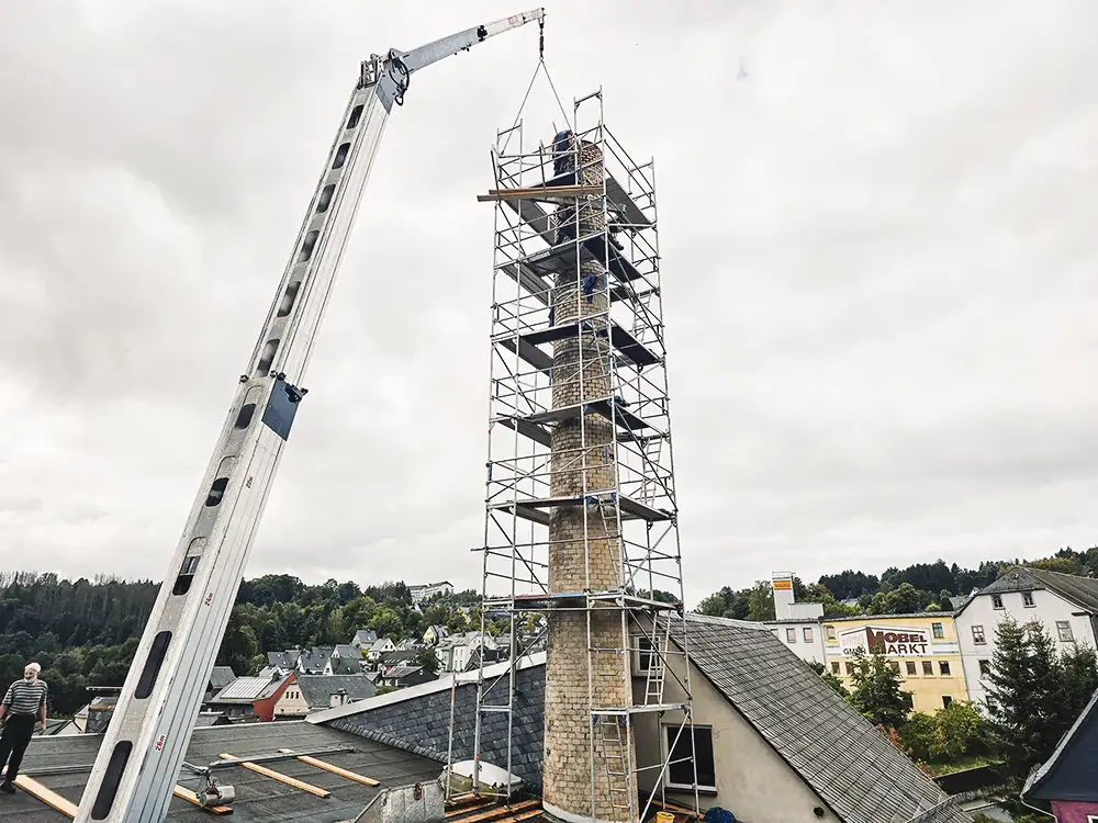 Curved dark slate roof with an attached rusty vertical pipe or antenna against a partly cloudy sky.
