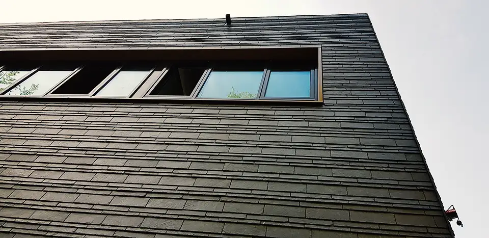 Curved dark slate roof with an attached rusty vertical pipe or antenna against a partly cloudy sky.